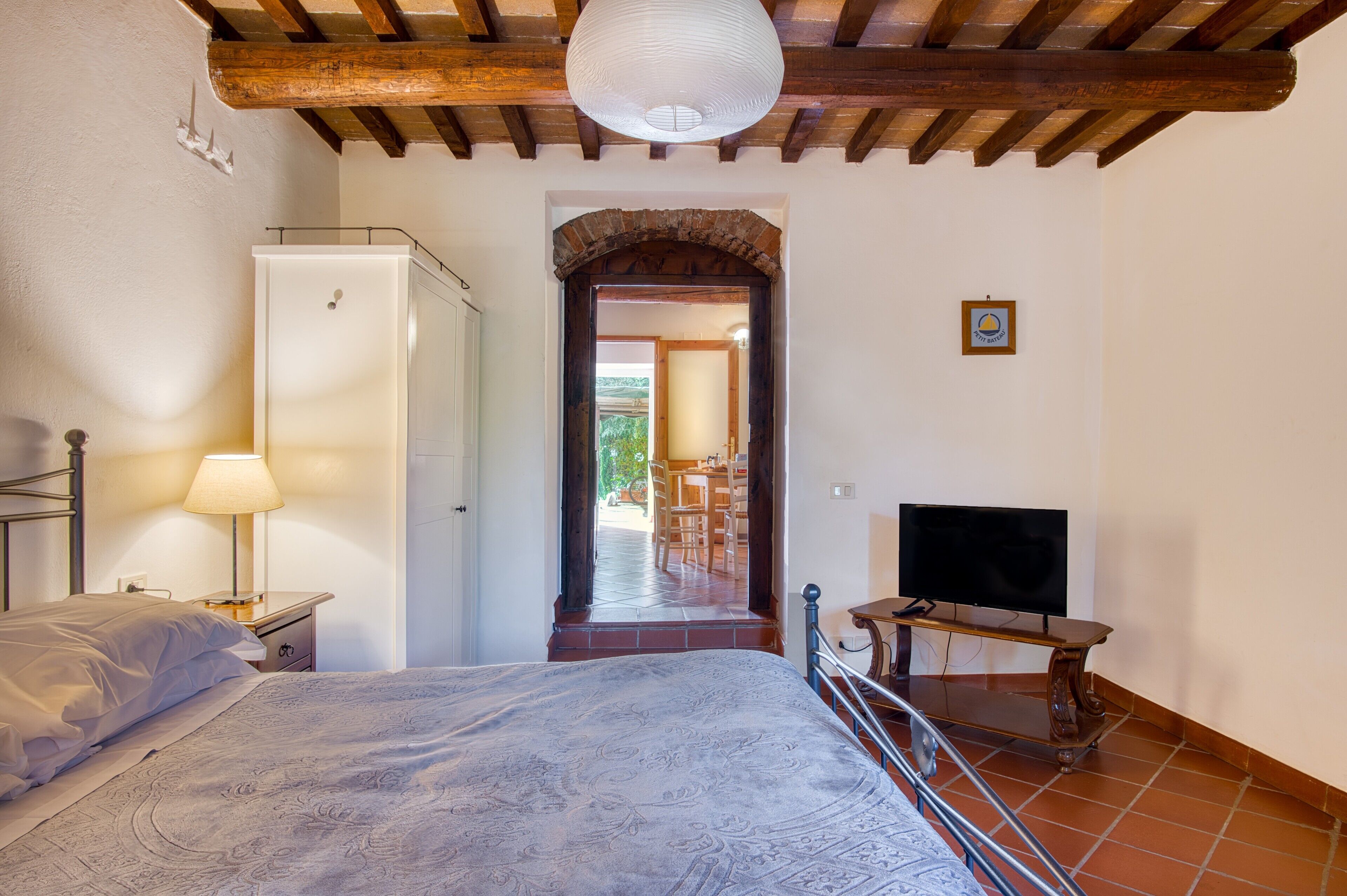 Une chambre à coucher avec un lit, une table de chevet avec une lampe, un téléviseur posé sur un meuble et un plafond en bois.