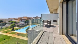 Un balcon doté d’une barrière en verre, donnant sur une piscine et une pelouse, avec une table et des chaises sur le côté droit.