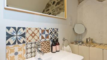 A bathroom with a white sink, patterned tiles, a mirror, and toiletries.