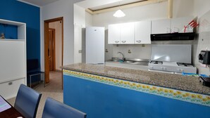 Una cocina compacta con estufa a gas, gabinetes blancos y una pared azul de acento.