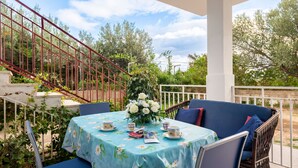 Un espacio de estar al aire libre cubierto, con una mesa lista para dos personas, sillas alrededor y una escalera que lleva a un nivel superior.