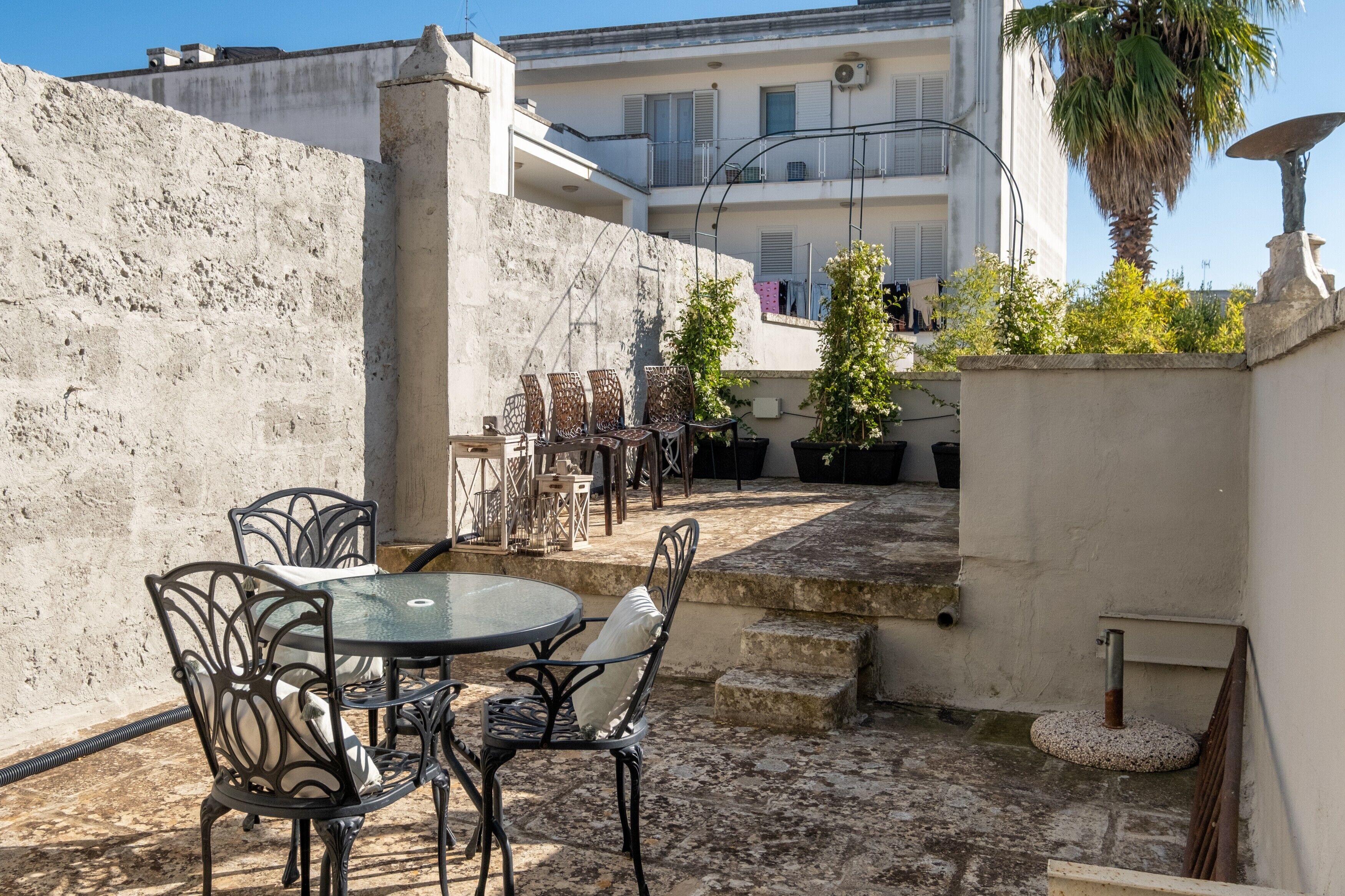 Une cour avec une table ronde et des chaises, un mur de pierre et un bâtiment en arrière-plan.