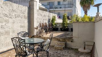 Une cour avec une table ronde et des chaises, un mur de pierre et un bâtiment en arrière-plan.