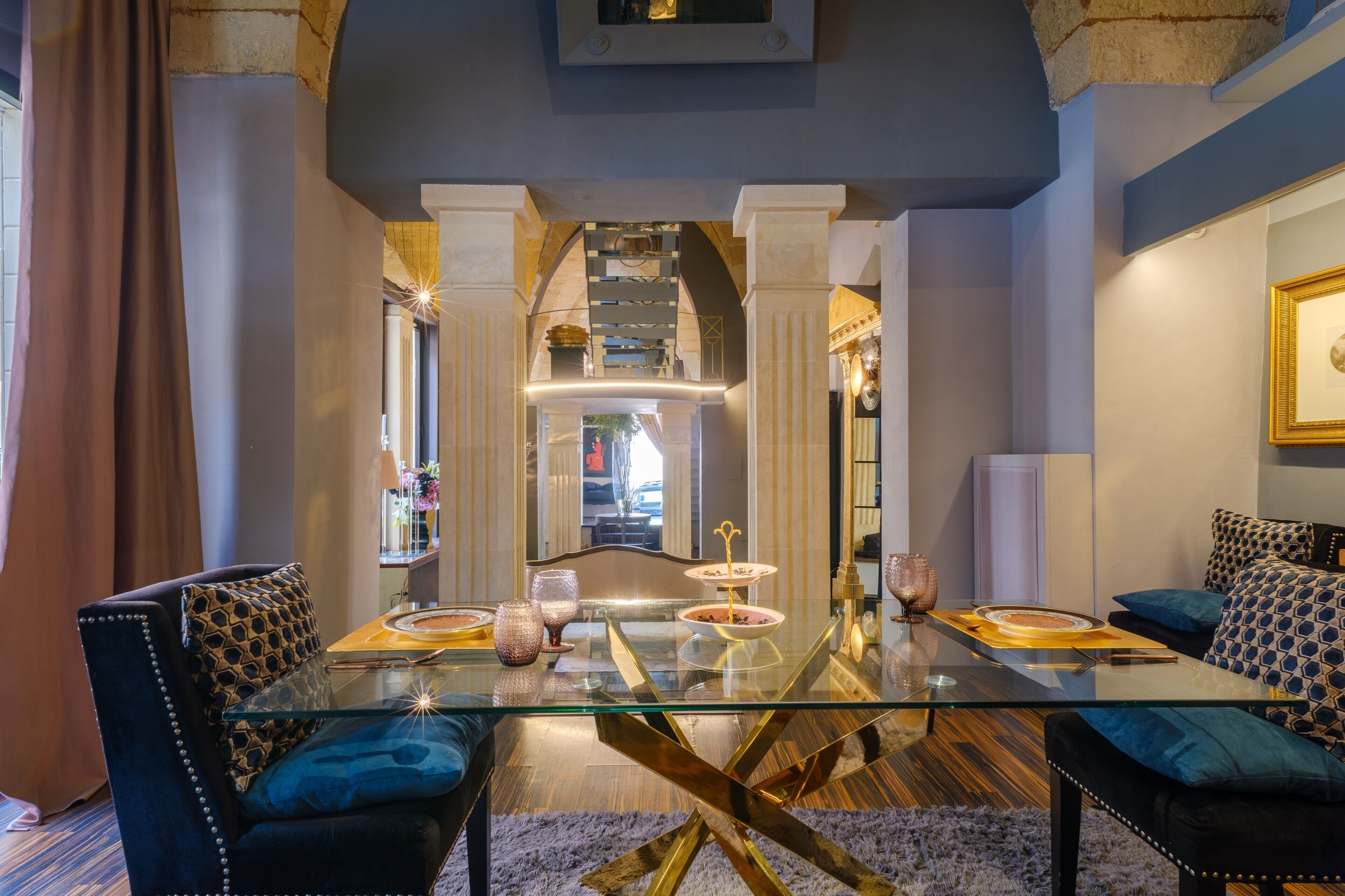 Un comedor moderno con una mesa de vidrio, sillas tapizadas y vistas a una escalera.