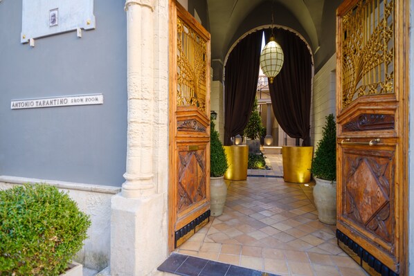 A hallway with ornate wooden doors, a sign for the Antonio Tarantino Show Room, and a tiled floor leading to a dark curtain backdrop.