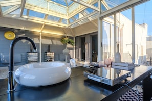 A modern kitchen with a large white sink, a built-in stove, and a glass-top dining table.