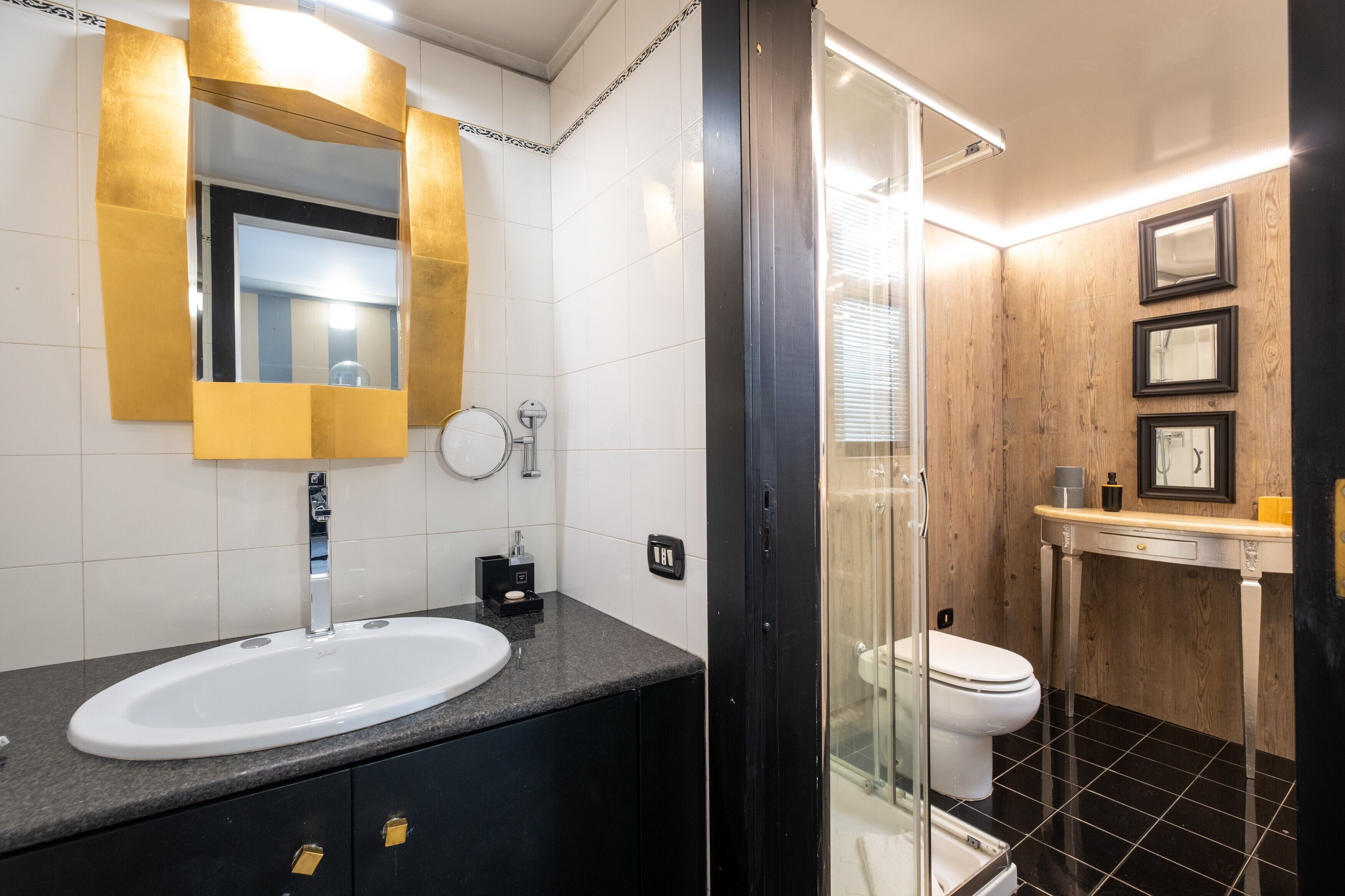 A modern bathroom with a white sink, a mirror with gold trim, a glass shower enclosure, and a toilet.