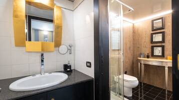 A modern bathroom with a white sink, a mirror with gold trim, a glass shower enclosure, and a toilet.