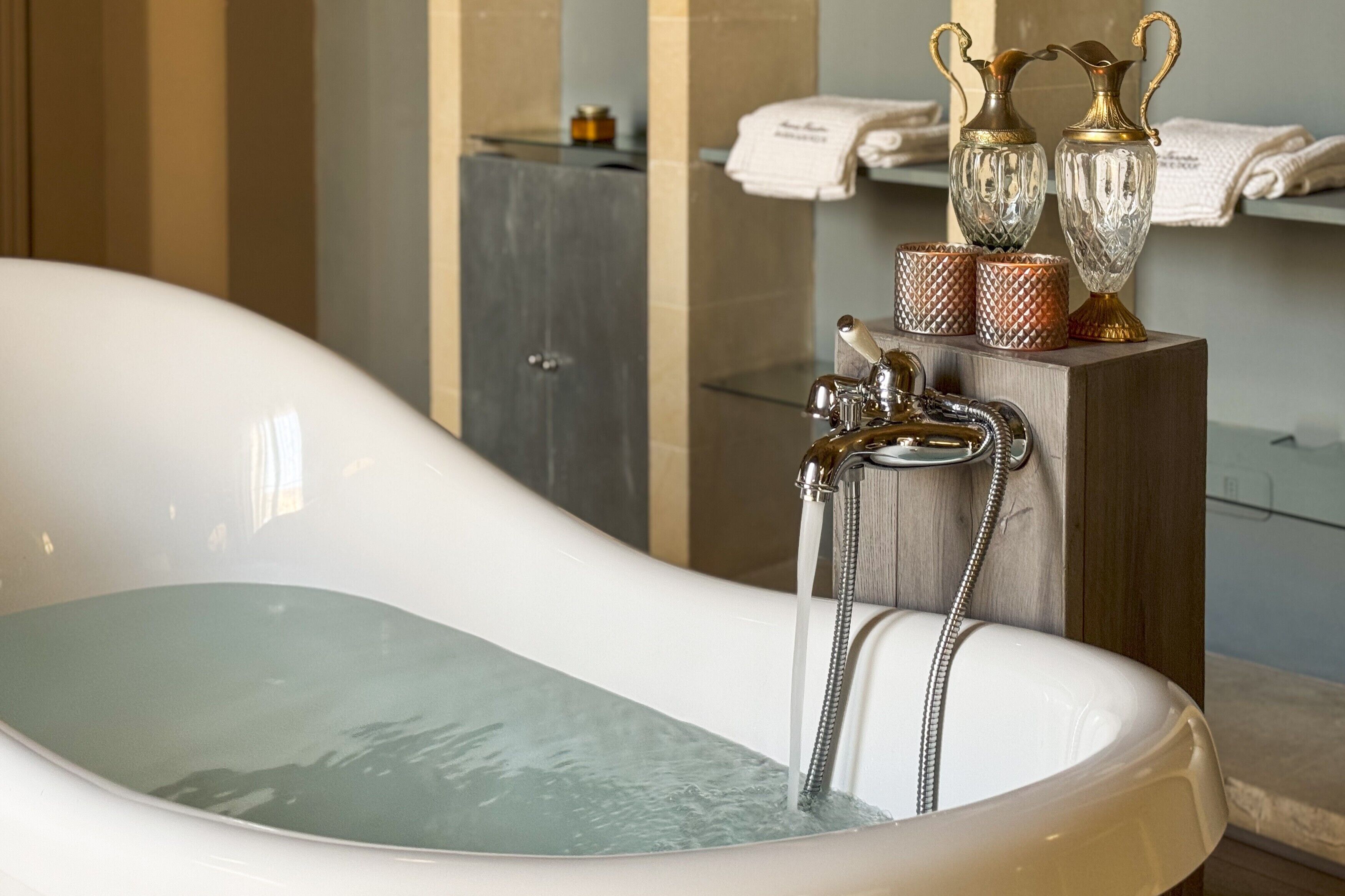 A bathtub with running water, a wooden stand with decorative items, and a towel rack in a bathroom.
