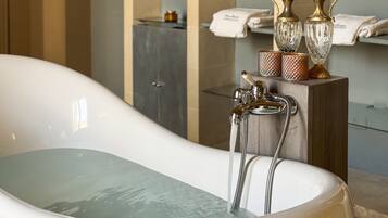A bathtub with running water, a wooden stand with decorative items, and a towel rack in a bathroom.