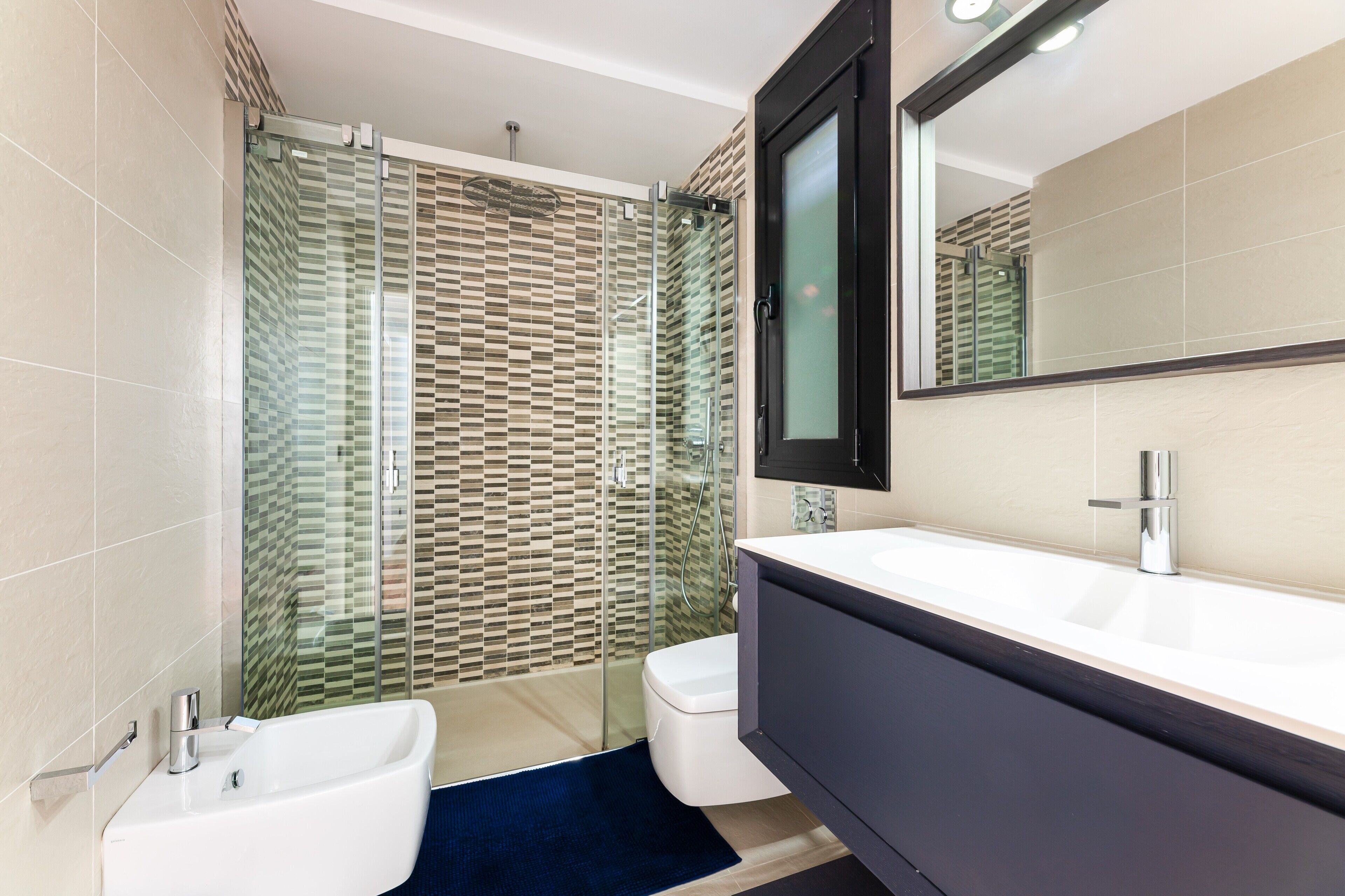 A modern bathroom with a glass shower enclosure, a white bathtub, and a large mirror above the sink.