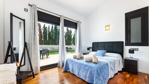 Een slaapkamer met een bed, nachtkastje, lamp, raam met gordijnen en uitzicht op de omgeving.