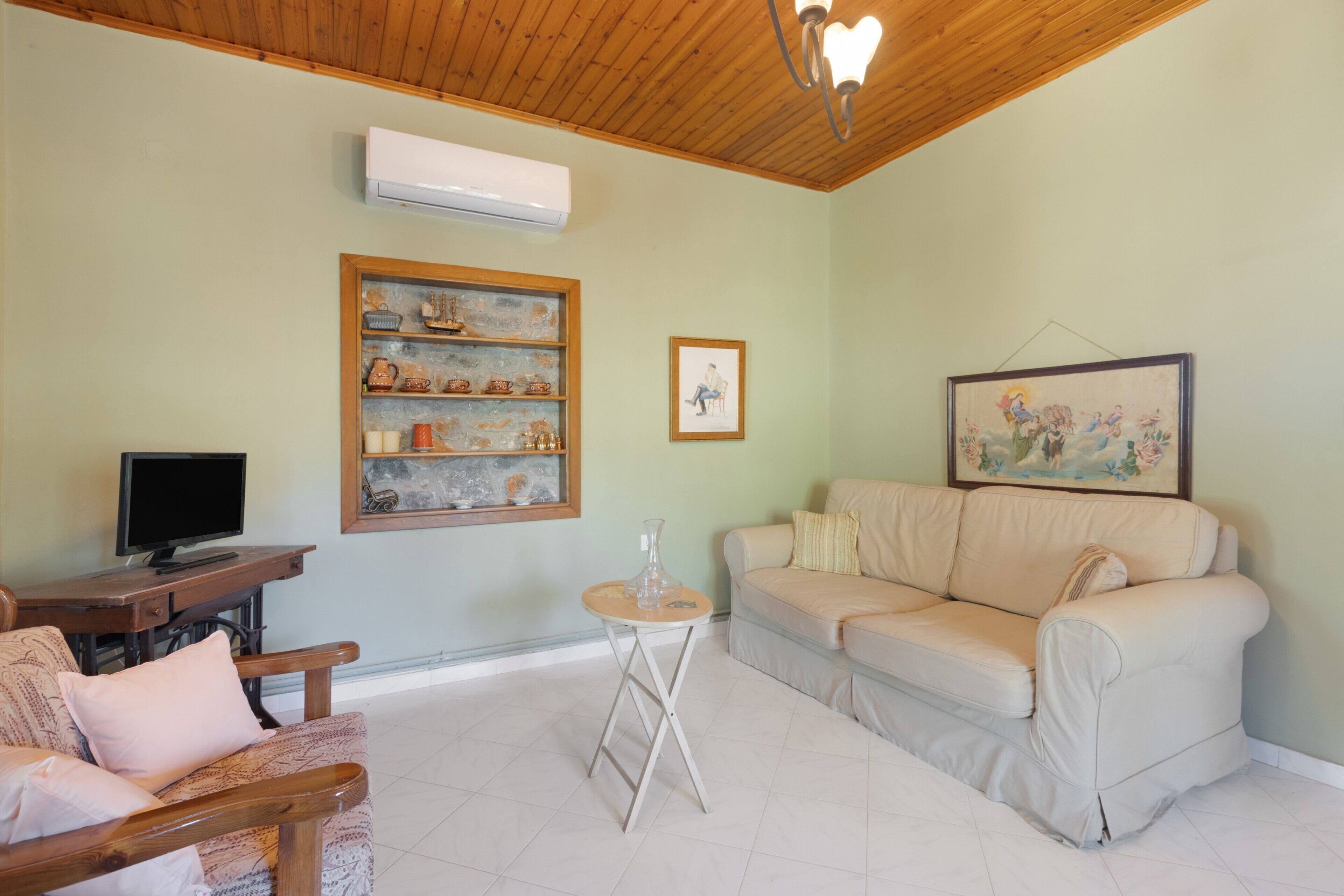 A living room with a wooden ceiling, a beige sofa, a wooden chair, a small table, and a television.
