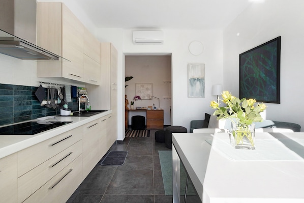 Une cuisine moderne avec des meubles de couleur bois clair, un plan de travail noir et un coin repas comprenant une table blanche et un vase de fleurs.
