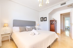 A bedroom with a large bed, two bedside tables with lamps, a wooden wardrobe, and a chandelier.