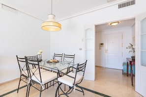 A dining area with a glass table and metal chairs, a hanging light fixture, and a white door in the background.