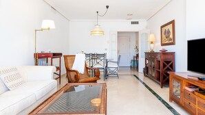 A living room with a sofa, a wooden coffee table, a dining table with chairs, a television, and a cabinet. - Spectacular Penthouse Puerto Romano with Sea View, Shared Pool & Wi-Fi (Marbella)