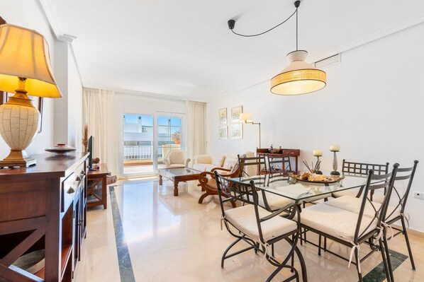 A dining area with a glass table, metal chairs, and a hanging light fixture.