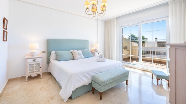 A bedroom with a large bed, a chandelier, a nightstand, and a view of the outside. - Spectacular Penthouse Puerto Romano with Sea View, Shared Pool & Wi-Fi (Marbella)