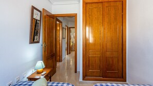 Un couloir avec un lit à motifs à carreaux, une porte en bois et une lampe sur une table de chevet.