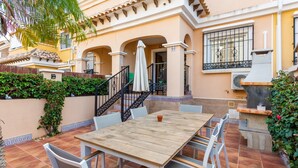 Une terrasse avec une table et des chaises en bois, un barbecue et un escalier menant à un balcon.