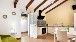 Un ambiente abitativo compatto con angolo cottura, zona pranzo e divano verde.
