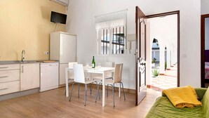 Una cucina moderna con elettrodomestici bianchi, un'area pranzo con tavolo e sedie e un divano verde con una coperta gialla.