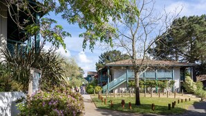 A building with a staircase leading to a porch, surrounded by greenery and a pathway. - Apartment "Bisbau" with Private Terrace, Private Garden & Shared Pools (Moliets-et-Maa)