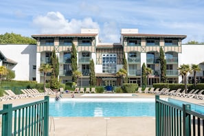 Un hôtel doté d’une piscine, de chaises longues et d’un bâtiment à deux étages avec des balcons.