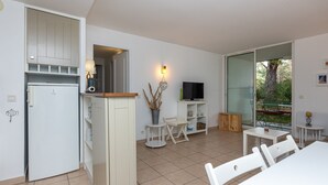 A modern kitchen with a built-in fridge, a dining area with a table and chairs, a TV, and a sliding glass door leading to a garden. - Apartment "Bisbau" with Private Terrace, Private Garden & Shared Pools (Moliets-et-Maa)