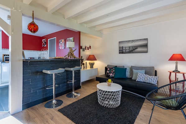 A modern living area with a kitchen, bar stools, a round coffee table, a sofa with cushions, and a red lamp.