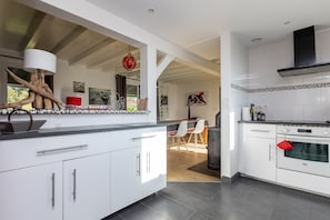 A modern kitchen with white cabinetry, a built-in oven, and a dining area with chairs.