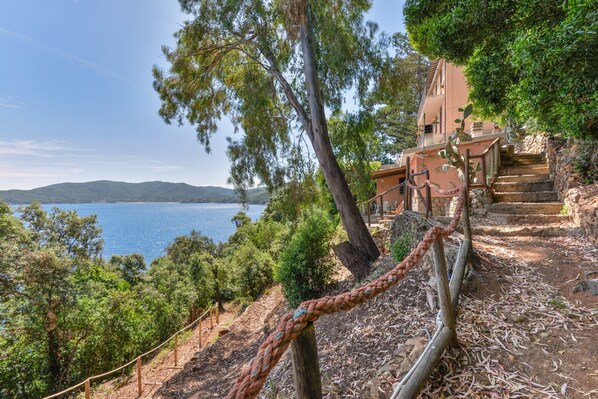 A coastal property with a staircase leading to a building, surrounded by trees and overlooking a body of water.