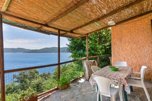 A covered outdoor seating area with a table and chairs, overlooking a body of water and hills.