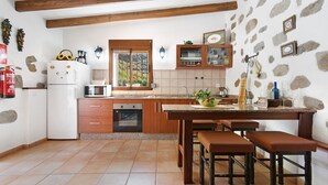 Cozinha com armários de madeira, geladeira branca, janela e parede de pedra.