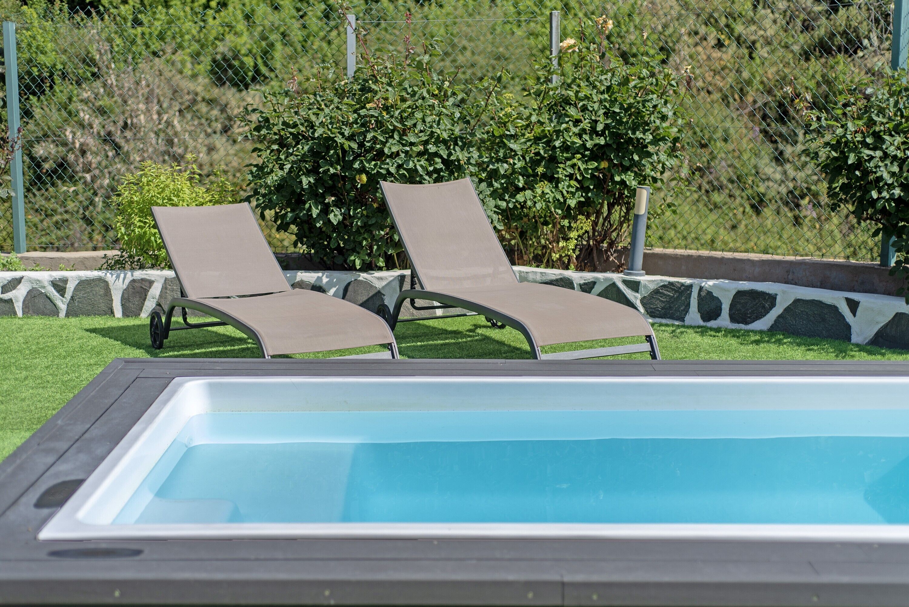 Une piscine avec deux chaises longues et une bordure en pierre.
