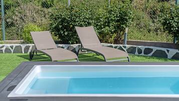 Une piscine avec deux chaises longues et une bordure en pierre.