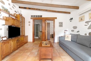 A living room with a television, wooden cabinets, a grey sofa, and a tiled floor.