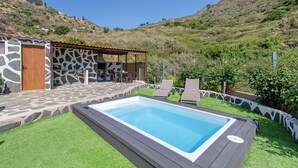 Piscina com um terraço de pedra, espreguiçadeiras e área de estar coberta ao ar livre.