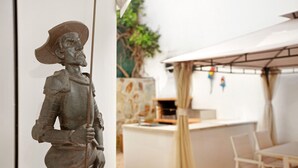 Una statua in una stanza con un tavolo e sedie bianchi, un bancone e una pianta.