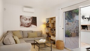 Un soggiorno con divano, tavolino, libreria e una grande finestra vista su un muro di pietra e piante.