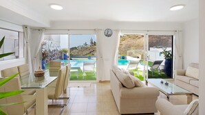Un'ampia zona giorno con un tavolo in vetro, divani color beige e vista su una piscina.