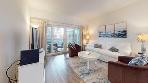 A modern living room with a sofa, armchair, and coffee table, a flat-screen TV, and a large window with curtains.