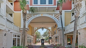 The entrance to The Village of Baytown Wharf with a brick facade, palm trees, and a clear sky.