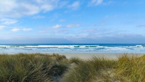 Una spiaggia con onde, dune erbose e cielo sereno.