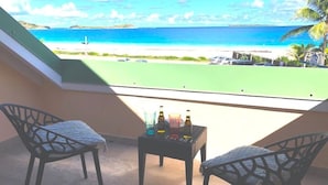 Un balcón con dos sillas y una mesita con bebidas, con vista a una playa y al océano.