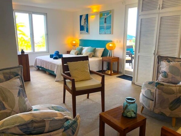 A spacious room with a bed, a chair, a small table, and a view of the outdoors.