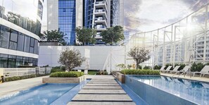 A modern outdoor swimming pool area with a clear sky, surrounded by high-rise buildings and lounge chairs. - LUX - The Pad Executive Suite 4 (Dubai)