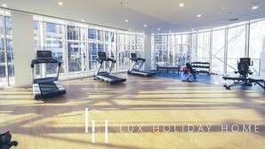 A spacious gym with treadmills, a rowing machine, and a weight bench. Large windows offer views of the city. - LUX - The Pad Executive Suite 4 (Dubai)