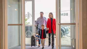 Una familia entrando en un edificio con puerta de vidrio, un cartel que dice 'SAÍDA' en la parte superior y un coche visible afuera.